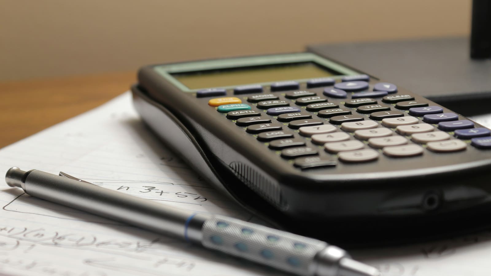 A calculator and a mechanical pencil resting on a page of handwritten calculations